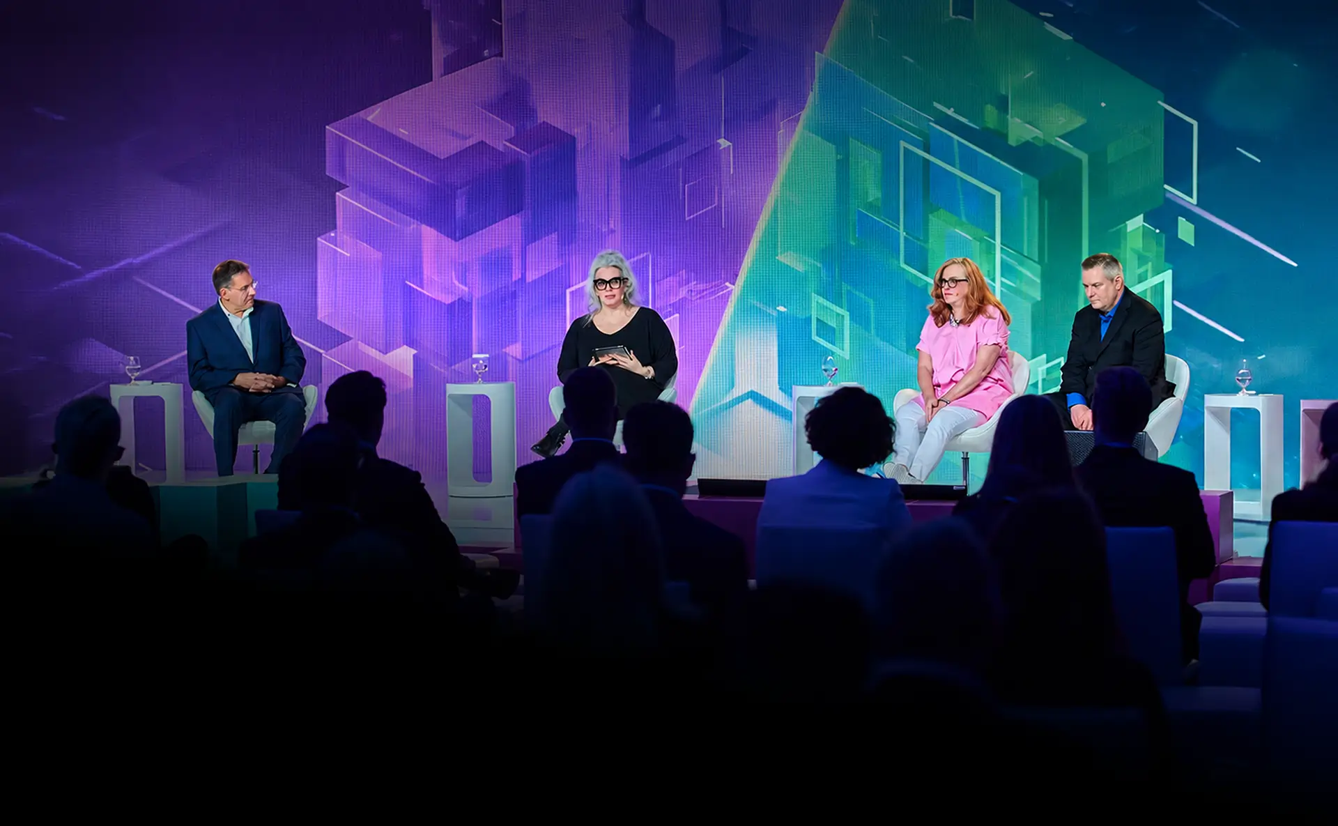 Four panellists in conversation on a conference stage in front of a purple and green backdrop, with the audience in the foreground.