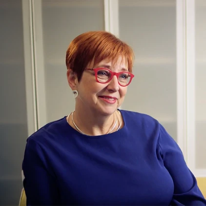 Portrait of a smiling woman with short red hair and glasses, in a blue dress