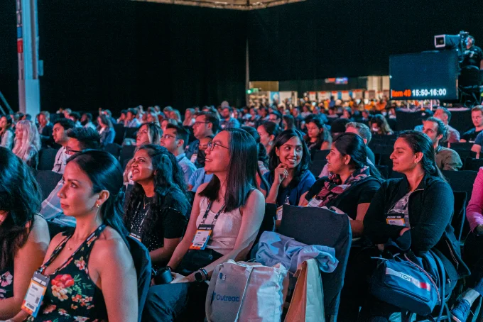 An audience watching a presentation in a large, dark hall