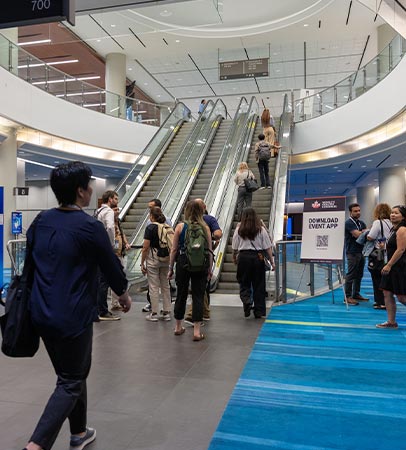 Attendees on escalators and walkways in a bright convention centre