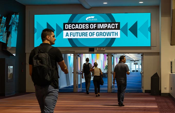 Attendees walking into a conference hall under a large Decades of Impact screen