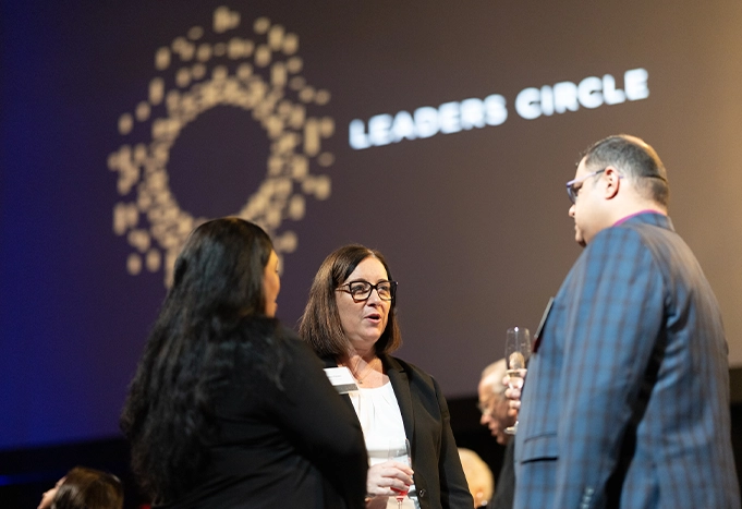 Guests talking at a Leaders Circle event, with the Leaders Circle logo behind them