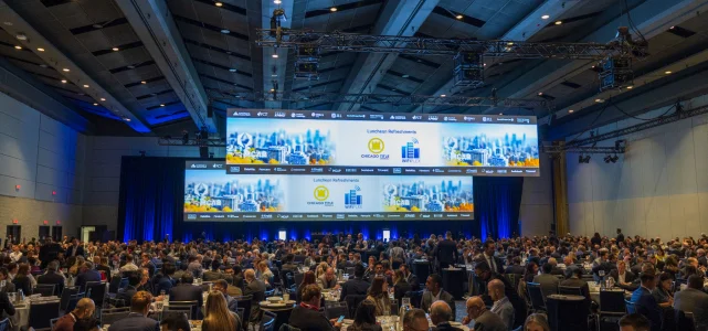 A large audience in a conference hall, facing the stage and screens