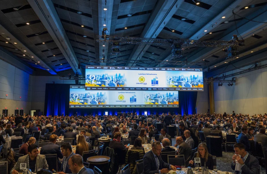 A full conference hall facing a stage with large screens
