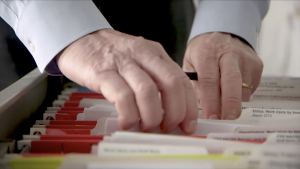 Hands flipping through paper files in a filing drawer