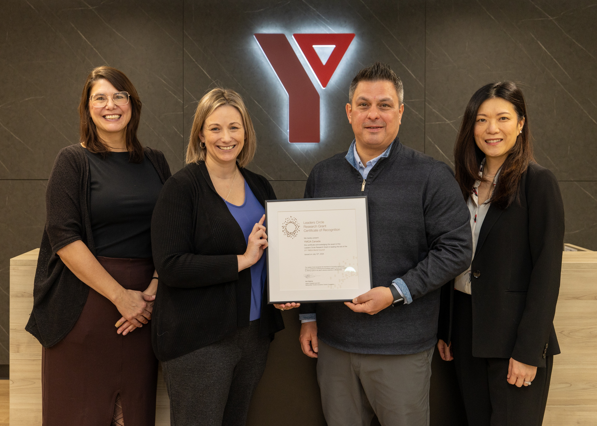 Four people posing with an award at a YMCA leadership event.