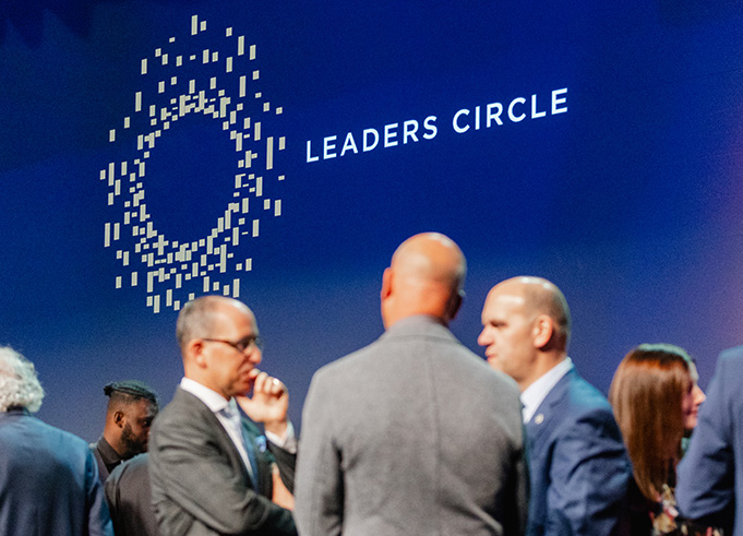 Business leaders talking in front of the Leaders Circle logo