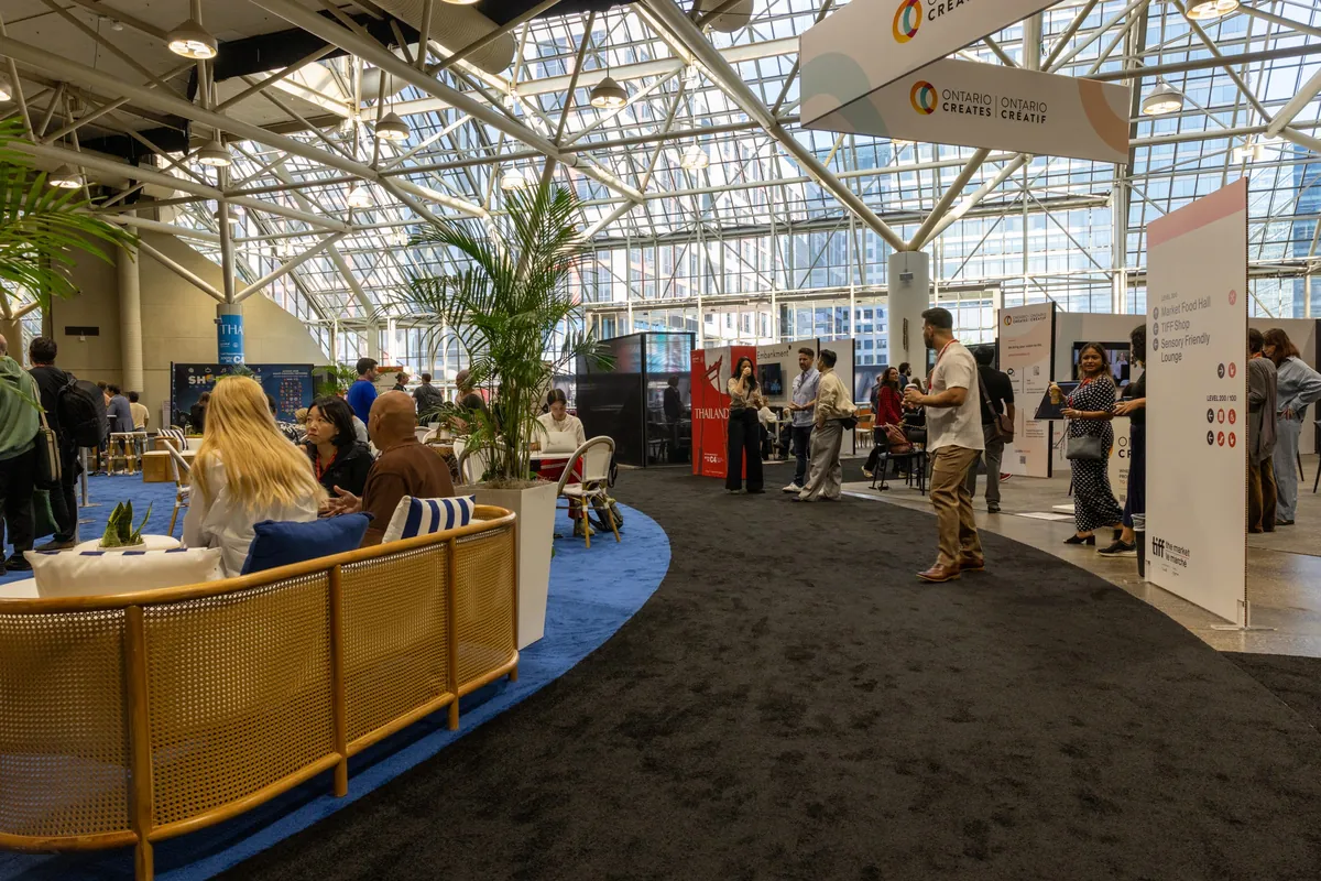 Attendees and exhibitors in a bright, glass-roofed convention hall with Ontario Creates signage