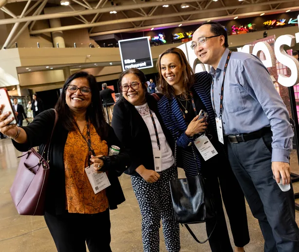 Group of four business and finance conference attendees posing together for a selfie.