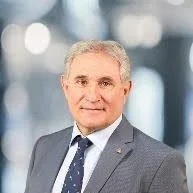Professional portrait of Louie DiPalma wearing a grey suit, white shirt and navy patterned tie.