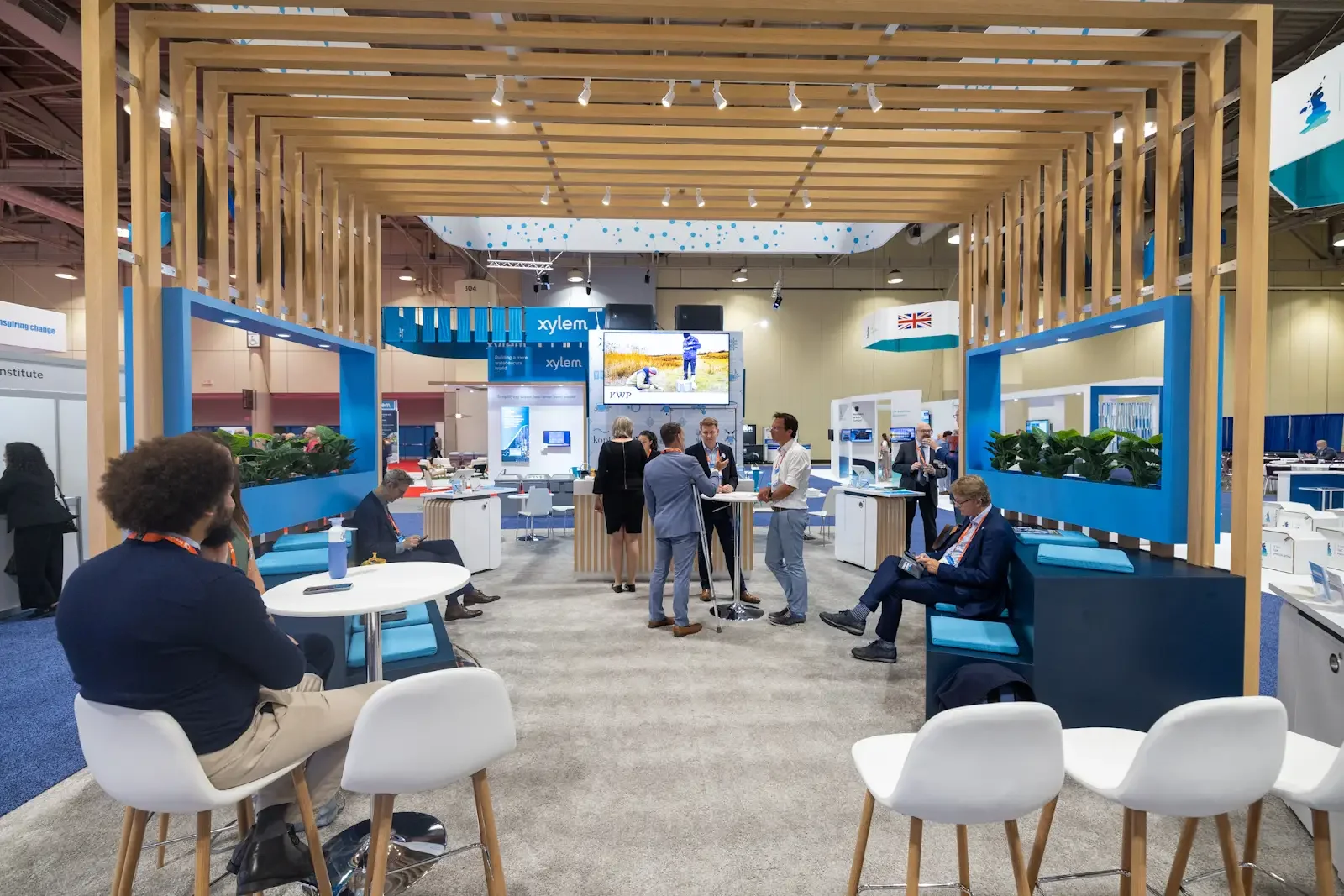 Conference exhibition hall with seating areas, exhibitor displays and attendees.