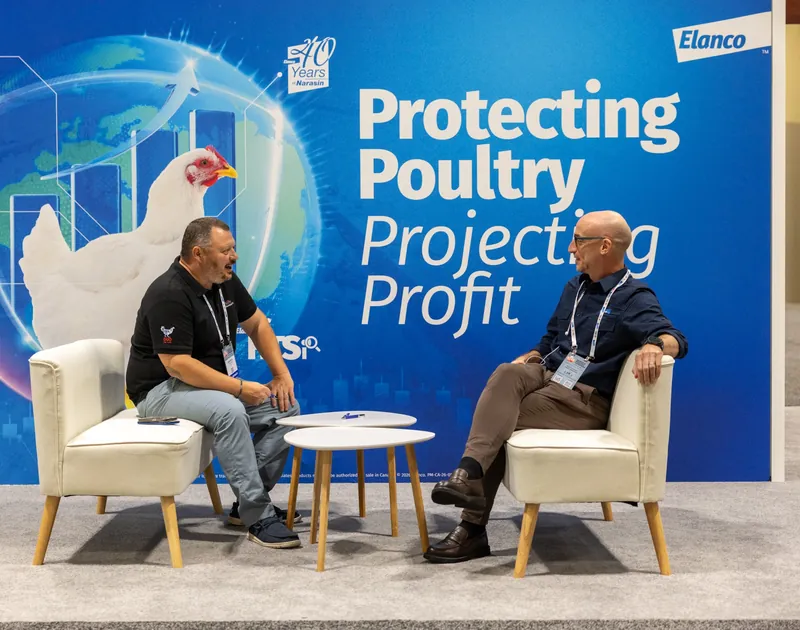 Two attendees in conversation seated in front of a blue poultry industry congress backdrop.