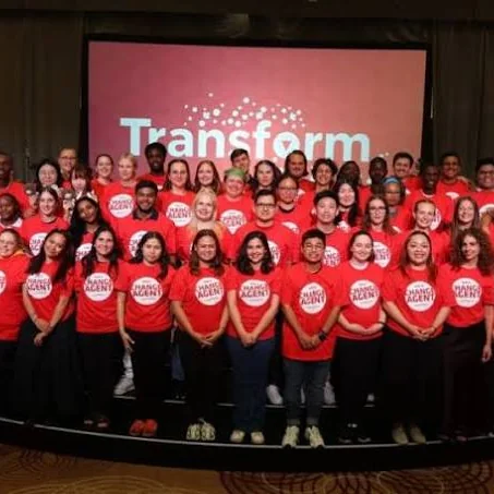 Large group of YMCA World Council participants standing together on stage in coordinated red “Change Agent” T-shirts, gathered on stage in front of a “Transform” screen